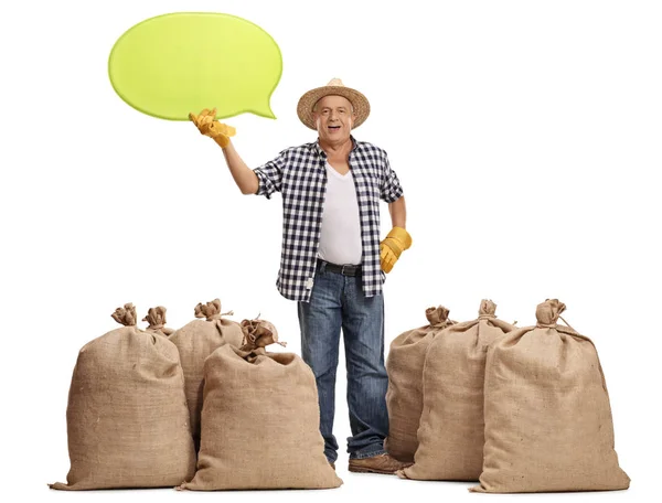 Farmer standing between burlap sacks and holding speech bubble — Stock Photo, Image