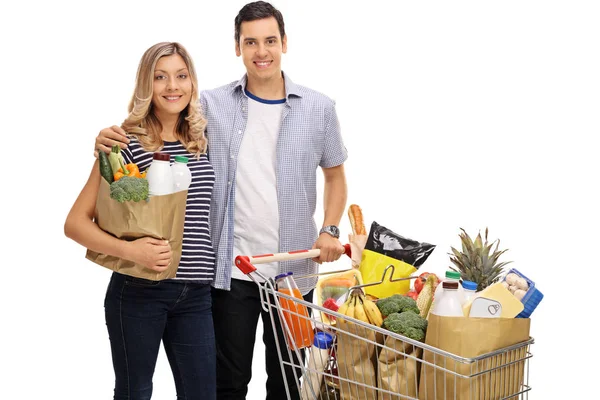 Coppia con una shopping bag e un carrello pieno di generi alimentari — Foto Stock