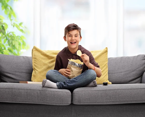 Niño sentado en un sofá y comiendo papas fritas — Foto de Stock