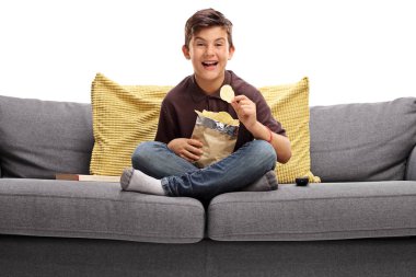 boy sitting on a sofa and eating potato chips