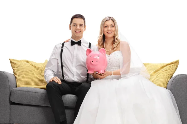 Pasangan pengantin baru duduk di sofa dan memegang celengan — Stok Foto