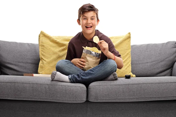 Niño sentado en un sofá y comiendo papas fritas — Foto de Stock