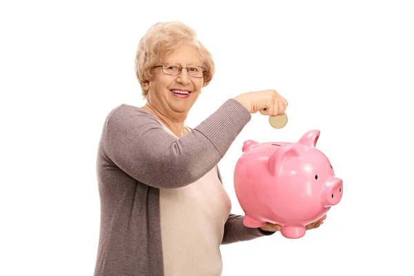 Äldre kvinna sätta ett mynt i en piggybank — Stockfoto