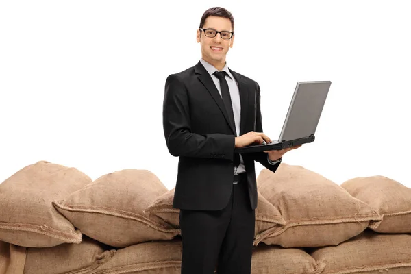 Zakenman met een laptop voor een stapel van jute zakken — Stockfoto