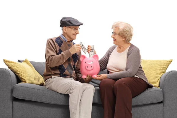 Пожилые люди сидят на диване и кладут деньги в копилку — стоковое фото