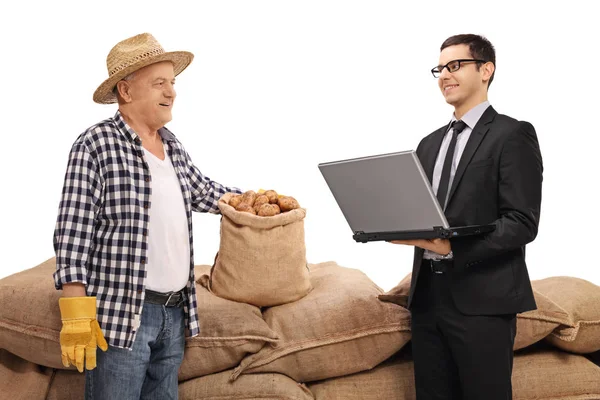 Agricoltore e uomo d'affari con un portatile di fronte a un mucchio di sacchi di iuta — Foto Stock