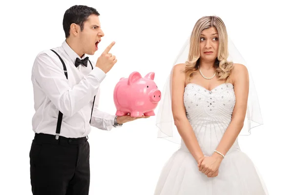 Boos bruidegom holding een spaarpot en schelden een verlegen brid — Stockfoto
