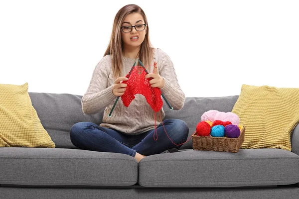 Chica confusa sentada en un sofá y tejiendo — Foto de Stock