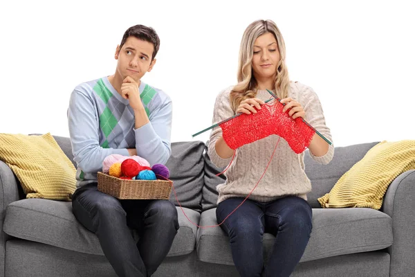 Bored guy sitting on a couch next to a woman knitting