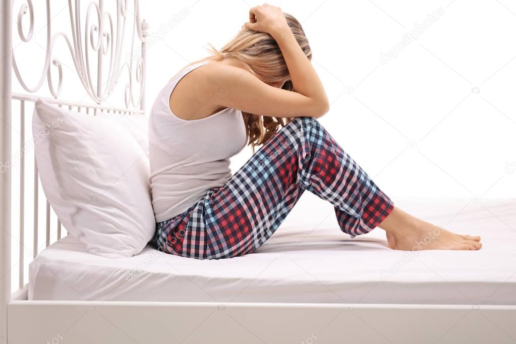 Sad woman sitting on a bed with her head down