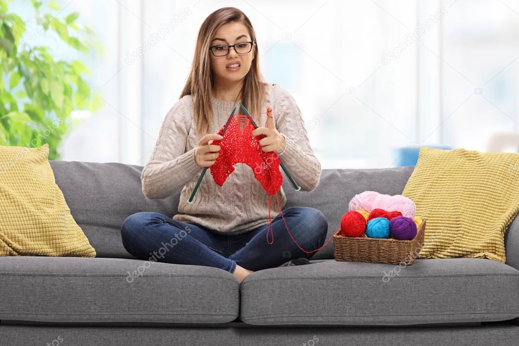 Confused young woman on a sofa knitting