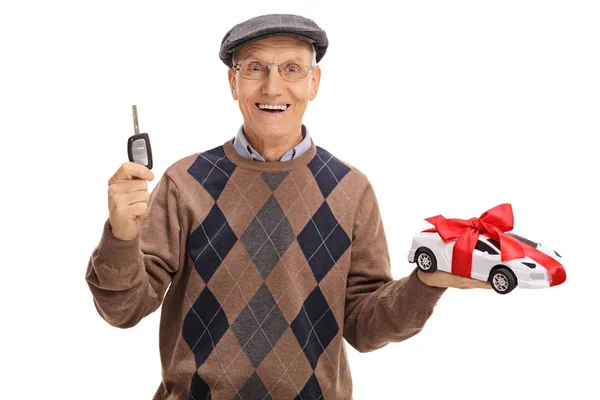 Senior holding a car key and a model car — Stock Photo, Image