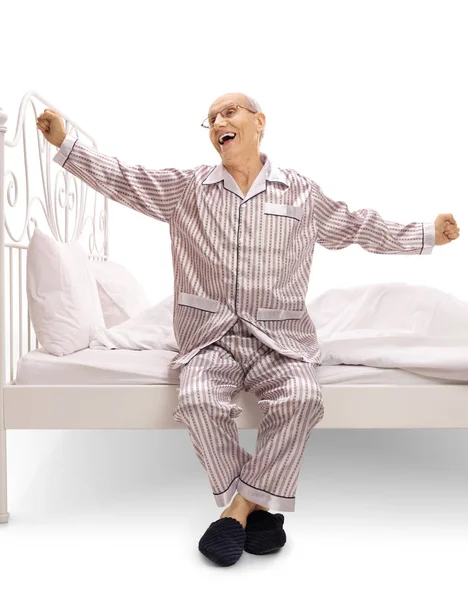 Äldre man i pyjamas sitter på en säng och gäspningar — Stockfoto