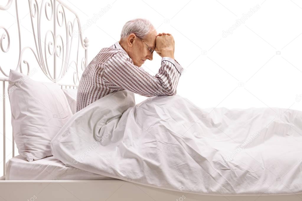 Depressed senior lying in bed with his head down