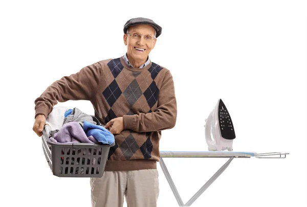 Sênior segurando cesta de roupa na frente da tábua de engomar — Fotografia de Stock