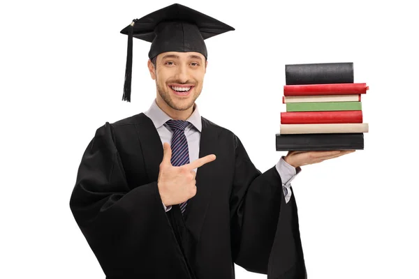 Estudiante graduado sosteniendo una pila de libros y señalando — Foto de Stock