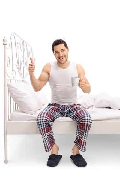 Man op bed holding cup en het geven van een duim omhoog — Stockfoto