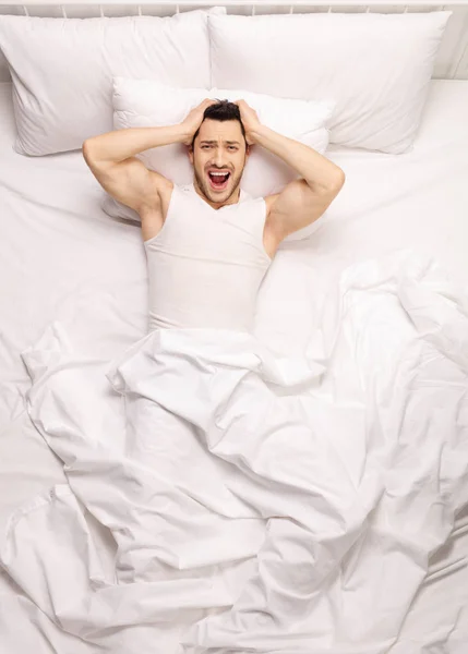 Разочарованный парень лежит в постели и кричит — стоковое фото