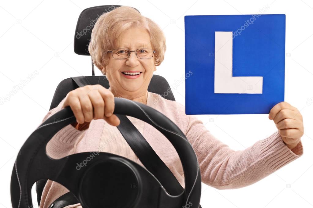 Happy mature woman sitting in a car seat and holding an L-sign isolated on white background