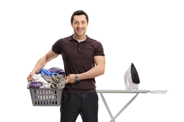 Guy holding a laundry basket in front of ironing board — Stock Photo, Image