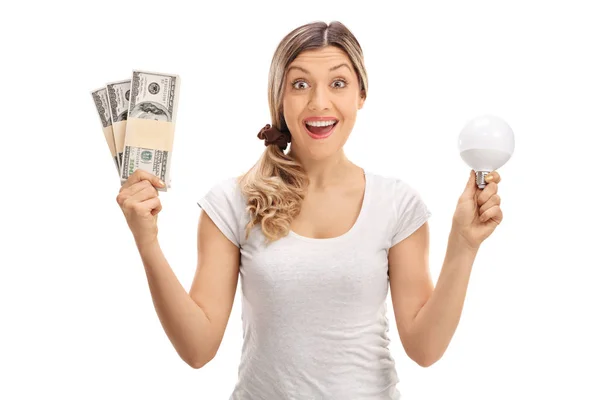 Женщина держит связки денег и светодиодную лампочку — стоковое фото