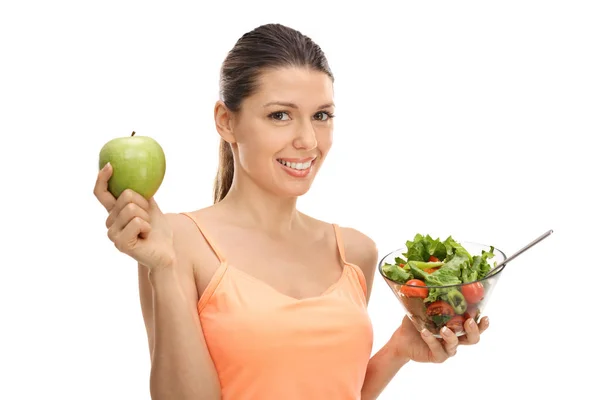 Mujer joven sosteniendo una manzana y una ensalada — Foto de Stock