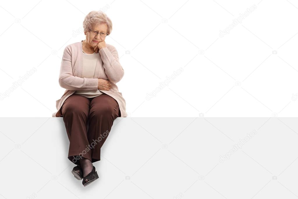 Pensive elderly woman sitting on a panel