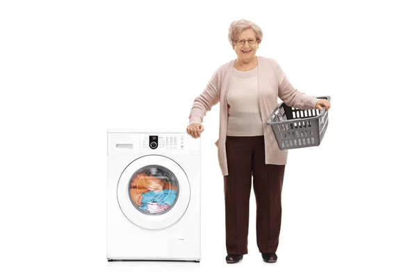 Elderly woman standing next to a washing machine — Stock Photo, Image