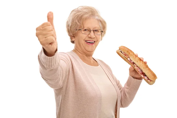 Пожилая женщина с бутербродом делает большой палец вверх вывеску — стоковое фото