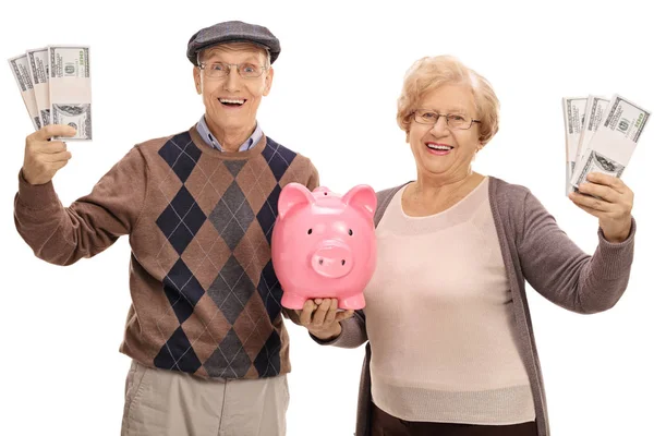 Пожилая пара с пачками денег и копилкой — стоковое фото