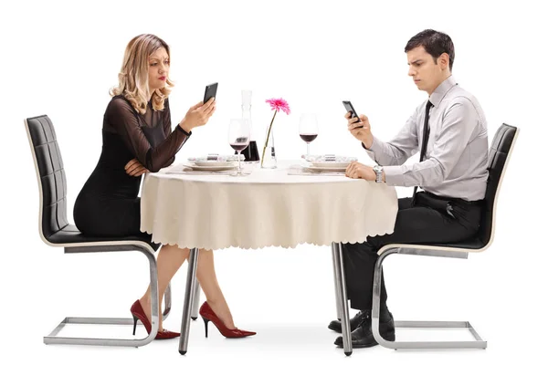 Мужчина и женщина за столом ресторана и смотрят на телефоны — стоковое фото
