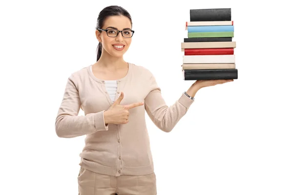 Female teacher holding a stack of books and pointing — Stock Photo, Image