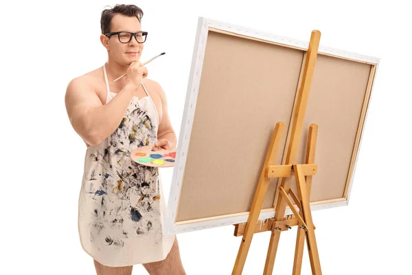 Pintor guapo usando un delantal y mirando un lienzo — Foto de Stock