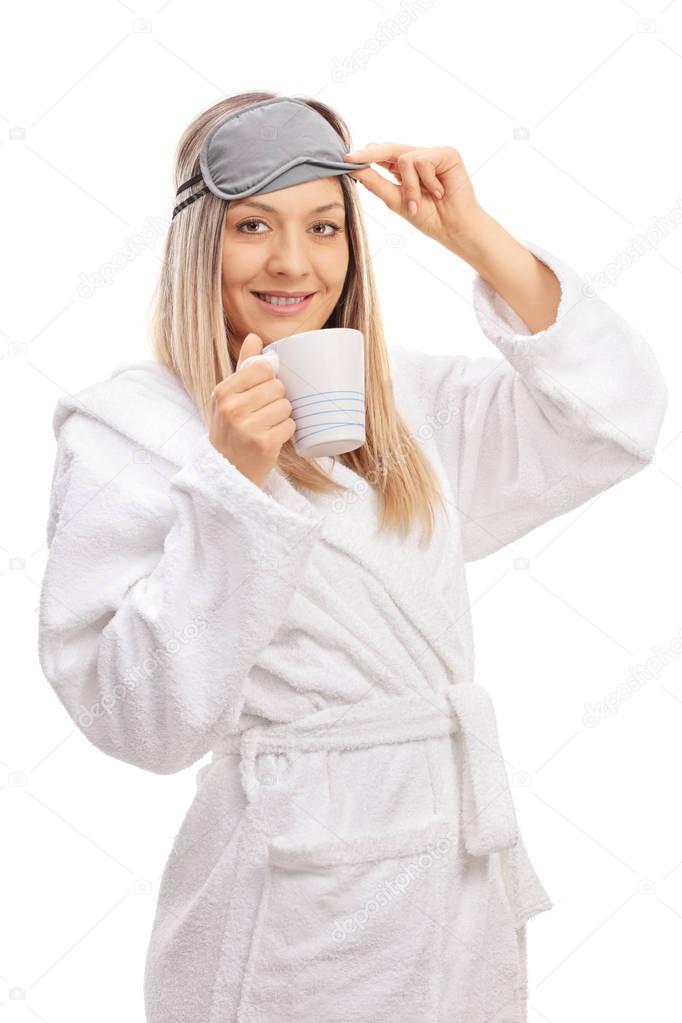 woman in a bathrobe with a sleeping mask and a cup