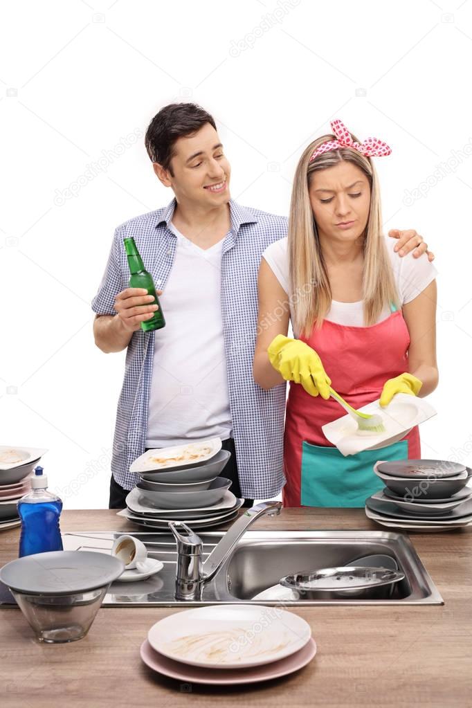 Man with beer hugging his wife doing the dishes