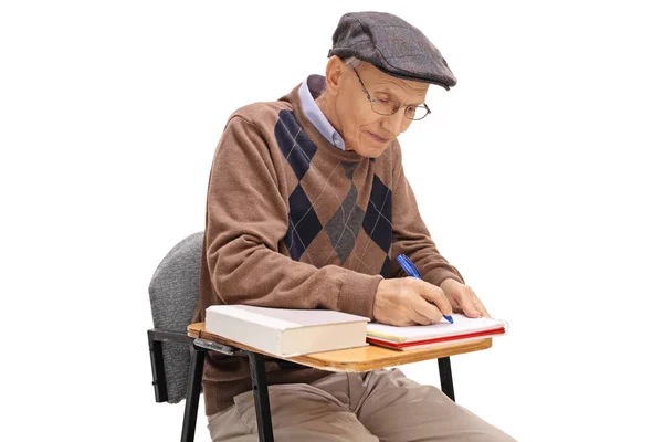 Пожилой студент сидит в школьном кресле и делает заметки — стоковое фото
