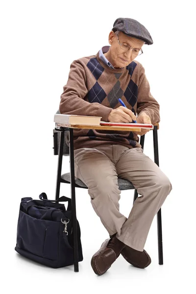 Зрелый мужчина в школьном кресле делает заметки — стоковое фото