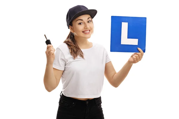 Meisje holding een auto sleutel en een L-teken — Stockfoto