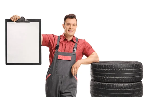 Mechanic leaning on pile of tires and holding blank clipboard — Stock Photo, Image