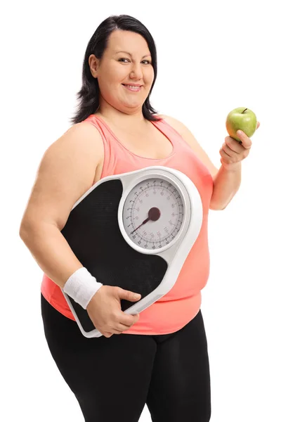 Mujer con sobrepeso sosteniendo una escala de peso y una manzana — Foto de Stock