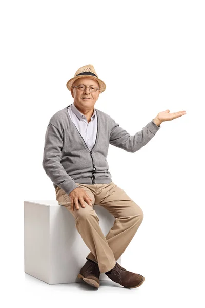 Senior sitting on a cube and gesturing with his hand — Stock Photo, Image