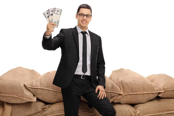 Affärsman som håller buntar av pengar framför säckväv säckar — Stockfoto
