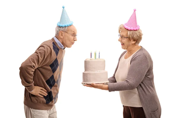 Femme âgée tenant gâteau d'anniversaire et homme âgé soufflant — Photo