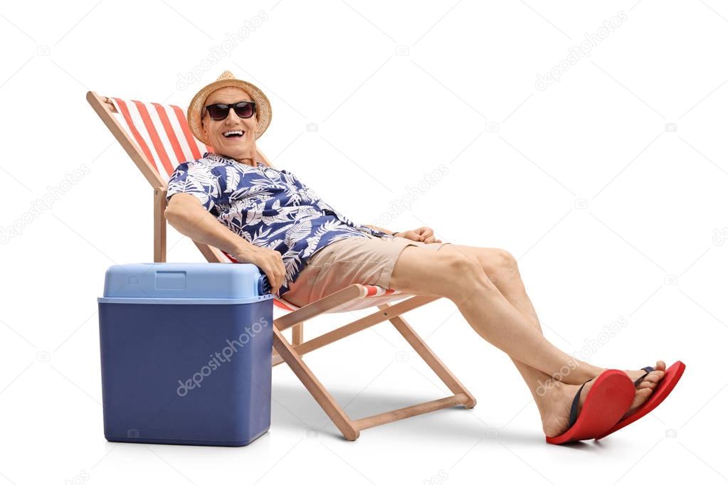 man sitting in a deck chair next to a cooling box
