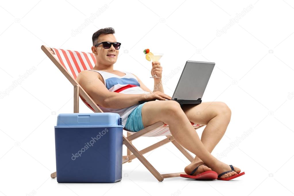 man with laptop and cocktail sitting in a deck chair