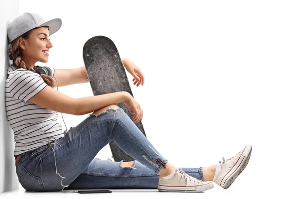Adolescente avec une planche à roulettes appuyée contre un mur — Photo