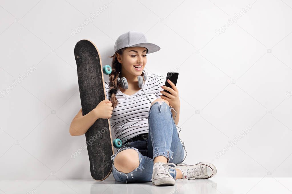 Teenage girl with a skateboard using a phone