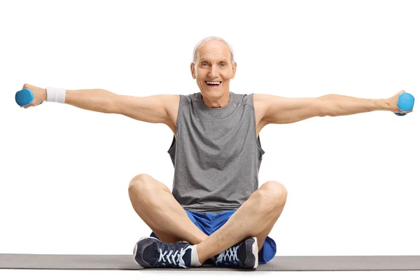 Man lifting dumbbells and sitting on an exercise mat — Stock Photo, Image