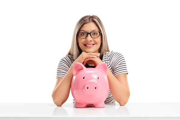 Young woman with a piggybank sitting at a table — Stock Photo, Image