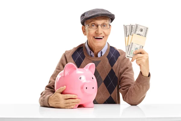 Senior met spaarpot en geld bundels aan een tafel — Stockfoto